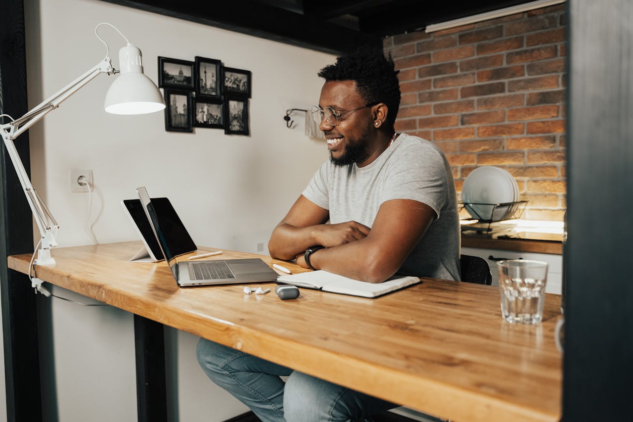 hero-services African American man smiling and working remotely from home using a laptop and digital tablet.